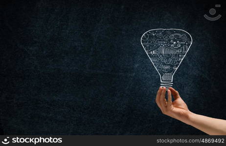 Light in darkness. Human hand on dark background holding light bulb