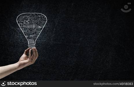Light in darkness. Human hand on dark background holding light bulb