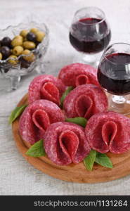 light meal snack from salami folded in the form of a flower with a glass sherry on a wooden dish. Close-up.