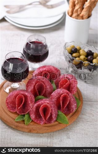 light meal snack from salami folded in the form of a flower with a glass sherry on a wooden dish.