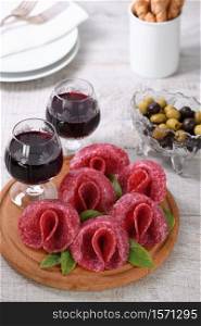light meal snack from salami folded in the form of a flower with a glass sherry on a wooden dish. Close-up.