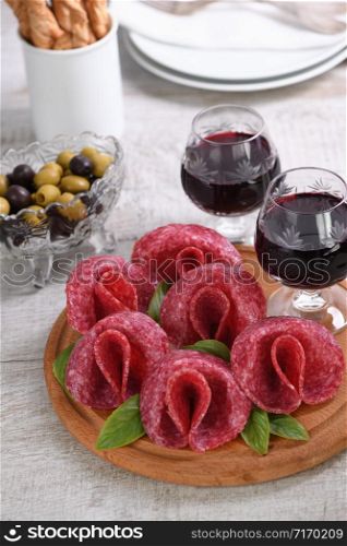 light meal snack from salami folded in the form of a flower with a glass sherry on a wooden dish.
