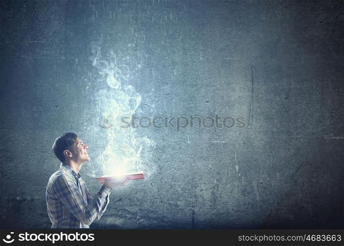 Light of education in darkness. Young man with book in hands and light out of pages