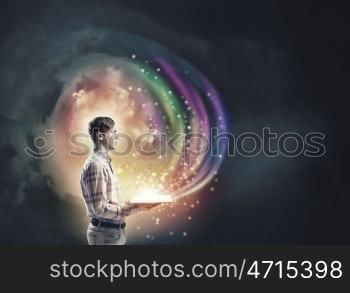 Light of education in darkness. Young man with book in hands and light out of pages