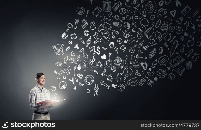 Light of education in darkness. Young man with book in hands and light out of pages