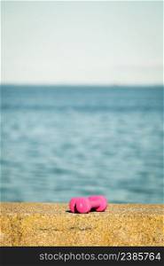 Light pink dumbbells sport symbol outdoor on sea shore. Active lifestyle bodybuilding.. Light pink dumbbells sport symbol outdoor on sea shore