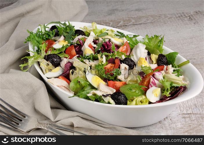 Light salad from the mix of lettuce leaves with tomatoes, eggs, slices of chicken breast and dried olives