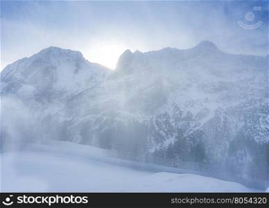 Light snow blizzard in the mountains - Winter alpine scenery with a soft blizzard that blows the fresh snow over the Austrian Alps mountains, while the sun is rising over the peaks.