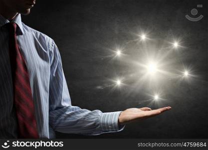 Light spot in darkness. Businessman holding light flash in palm on dark background