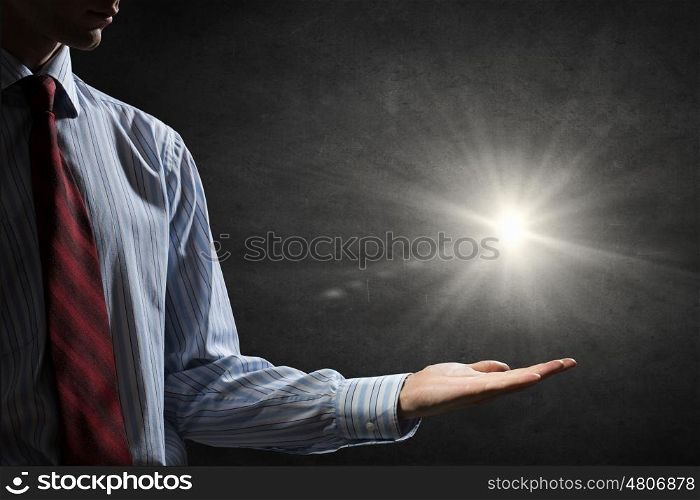Light spot in darkness. Businessman holding light flash in palm on dark background