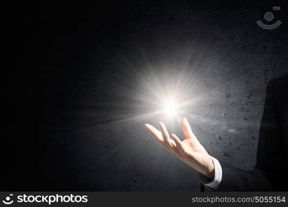 Light spot in darkness. Businessman holding light flash in palm on dark background