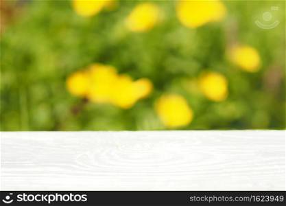 light wood table top on a background of blurred green grass and yellow flowers. no focus.