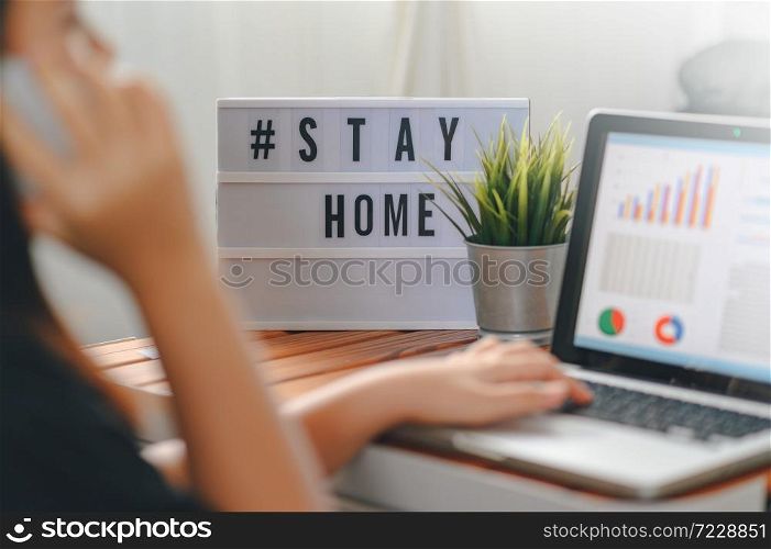 lightbox with text hashtag #STAYHOME glowing in lightand blurred woman working at home. Office worker on quarantine. Home working to avoid virus disease. Freelancer or remote worker concept.