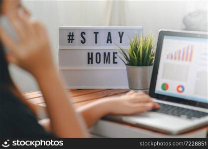 lightbox with text hashtag #STAYHOME glowing in lightand blurred woman working at home. Office worker on quarantine. Home working to avoid virus disease. Freelancer or remote worker concept.
