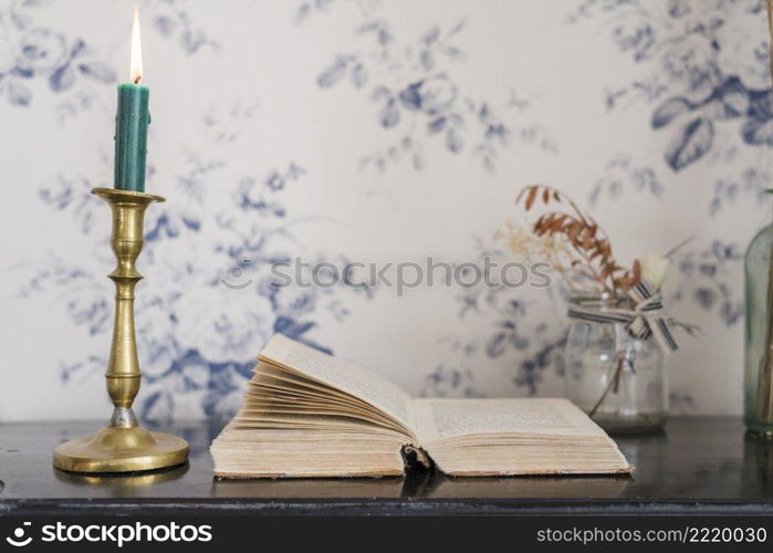 lighted candle candlestick holder open book desk against wallpaper