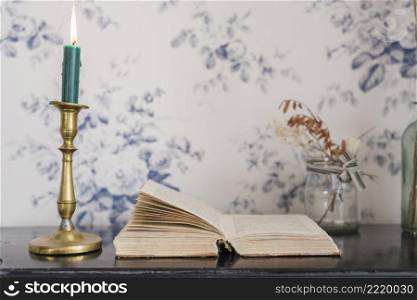 lighted candle candlestick holder open book desk against wallpaper