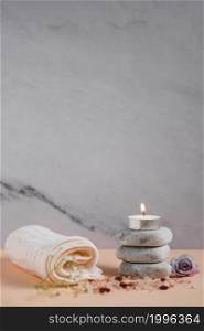 lighted candle spa stones with napkin rose himalayan salts peach colored backdrop against grey background