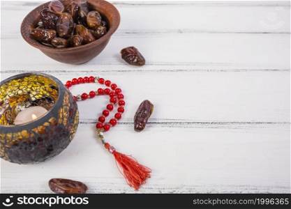 lighted candle with bowl juicy dates red prayer beads white wooden background