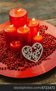 Lighted candles with red colored pearls around on a wooden table