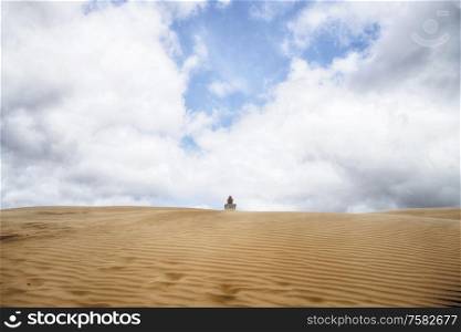 Lighthouse buried in a large sand dune under a blue cloudy sky in a desert