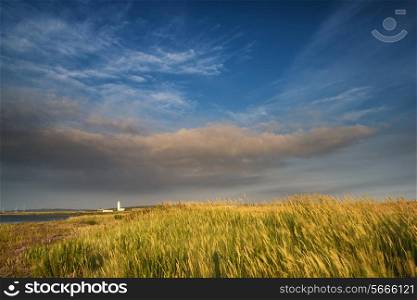 Lighthouse in landscape under dramatic stormy sky sunset