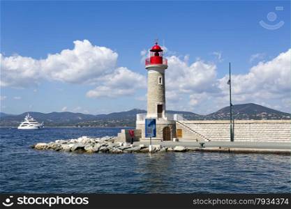 Lighthouse of the Port of St. Tropez, in the French Riviera, with a yacht in the background.