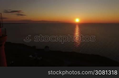 Lighthouse on a sunset background in the sea in summer. Aerial flying of the drone past the lighthouse at sunset. Lighthouse gives light signals to ships in the sea