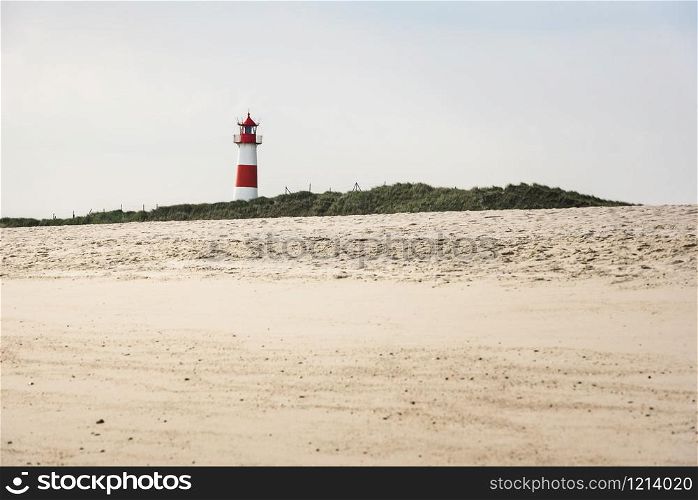 Lighthouse on grassy dunes and beach with yellow sand, on Sylt island, at the North Sea, Germany. Sunny summer beach landscape with beacon and sand.