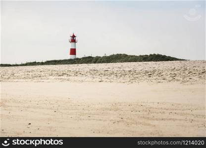 Lighthouse on grassy dunes and beach with yellow sand, on Sylt island, at the North Sea, Germany. Sunny summer beach landscape with beacon and sand.