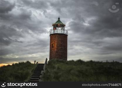 Lighthouse on hills with marram grass and old stairs, in the evening, on Sylt island, at North Sea, Germany. Beacon on grassy hill in northern Europe