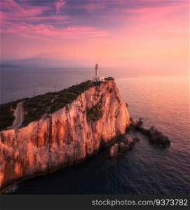 Lighthouse on the mountain peak at colorful sunset in summer. Aerial view. Beautiful lighthouse on the rock, cliffs, sea and sky with pink and purple clouds. Top view of Cape Lefkada, Greece. Beacon