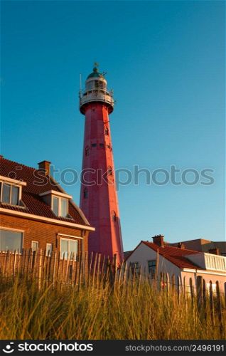 Lighthouse on the Netherlands coast among rural houses, vintage fence and grass