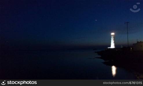 Lighthouse on the water edge near sea at night, timelapse