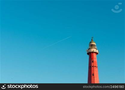 Lighthouse over blue sky background with airplane traces and copy space
