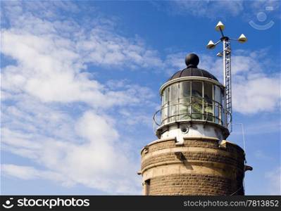 Lighthouse with the fresnel lens housing the lamp and a weather station at day.