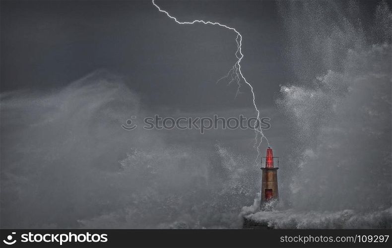 Lightning and wave over old lighthouse and pier of Viavelez in Asturias, Spain.