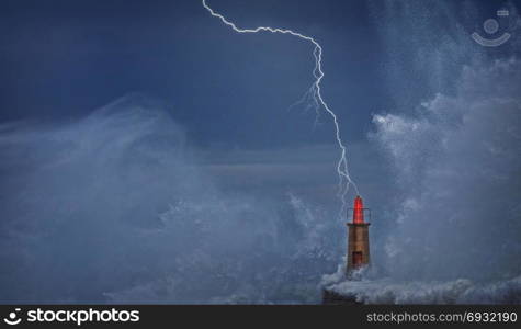 Lightning and wave over old lighthouse and pier of Viavelez in Asturias, Spain.