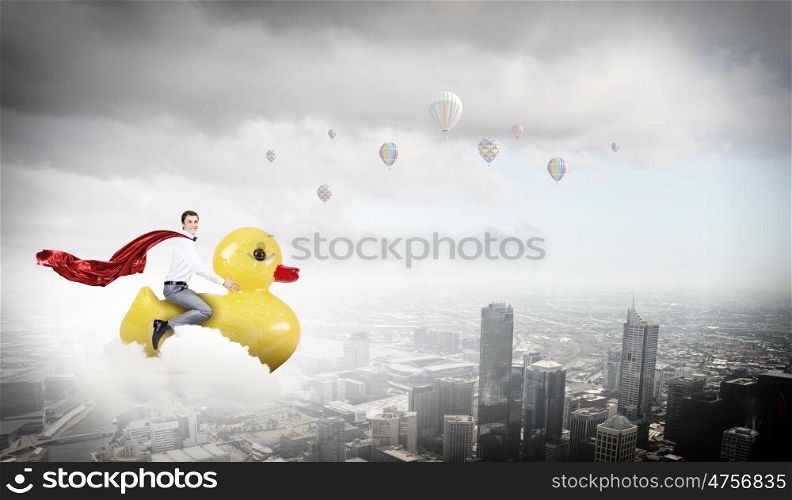 Like a child again. Young happy businessman riding yellow rubber duck