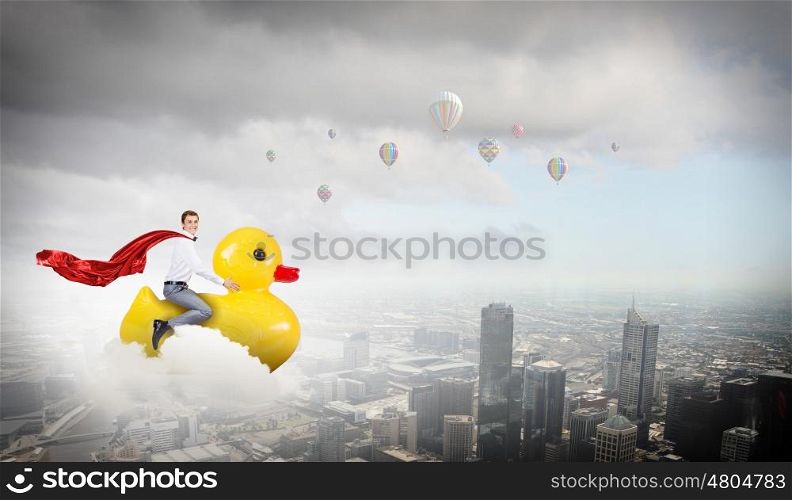 Like a child again. Young happy businessman riding yellow rubber duck