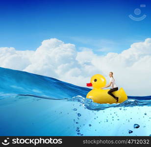 Like a child again. Young happy businesswoman riding yellow rubber duck