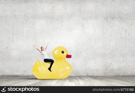 Like a child again. Young happy businesswoman riding yellow rubber duck