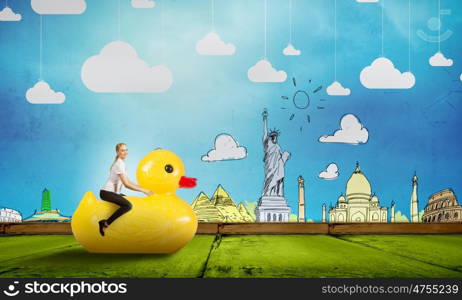 Like a child again. Young happy businesswoman riding yellow rubber duck