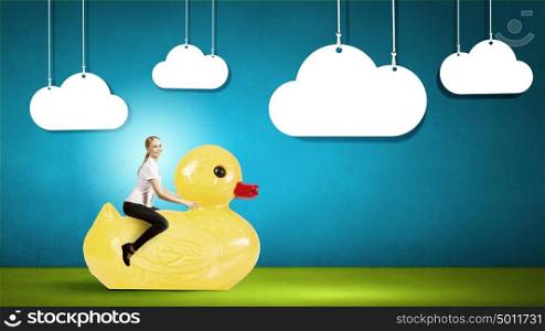 Like a child again. Young happy businesswoman riding yellow rubber duck