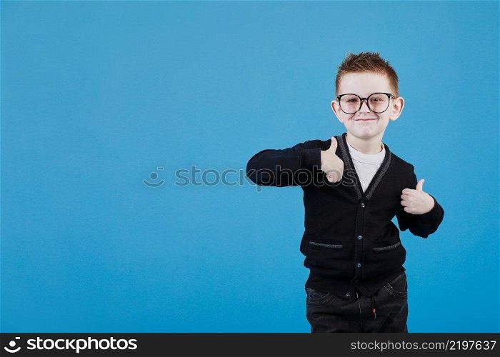 Like. Portrait of happy litt≤schoolboy with glasses smiling at camera and doing thumbs up≥sture, showing agree cool approval sign. indoor studio shot isolated on blue background.. Like. Portrait of happy litt≤schoolboy with glasses smiling at camera and doing thumbs up≥sture, showing agree cool approval sign. indoor studio shot isolated on blue background