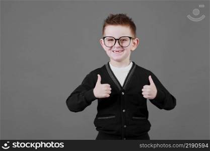 Like. Portrait of happy little schoolboy with glasses smiling at camera and doing thumbs up gesture, showing agree cool approval sign. indoor studio shot isolated on gray background.. Like. Portrait of happy little schoolboy with glasses smiling at camera and doing thumbs up gesture, showing agree cool approval sign. indoor studio shot isolated on gray background