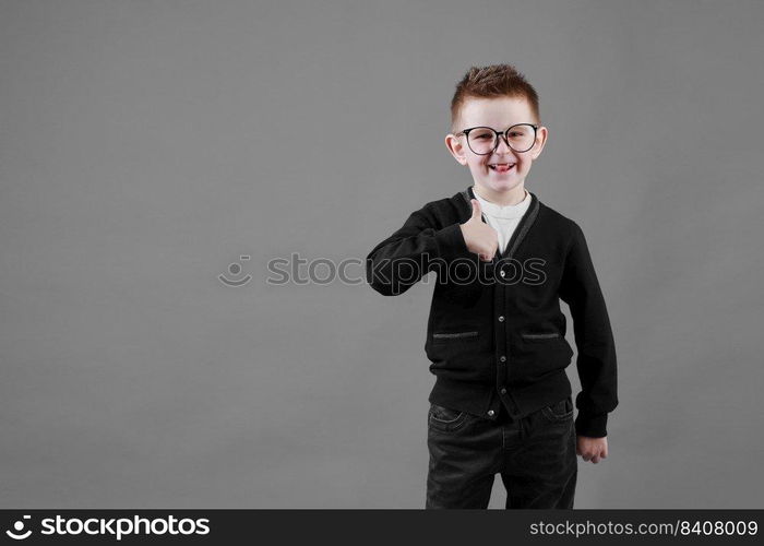 Like. Portrait of happy little schoolboy with glasses smiling at camera and doing thumbs up gesture, showing agree cool approval sign. indoor studio shot isolated on gray background.. Like. Portrait of happy little schoolboy with glasses smiling at camera and doing thumbs up gesture, showing agree cool approval sign. indoor studio shot isolated on gray background