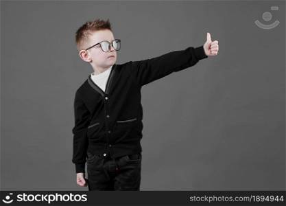 Like. Portrait of little schoolboy with glasses smiling at camera and doing thumbs up gesture, showing agree cool approval sign. indoor studio shot isolated on gray background. copy space. Like. Portrait of little schoolboy with glasses smiling at camera and doing thumbs up gesture, showing agree cool approval sign. indoor studio shot isolated on gray background. copy space.