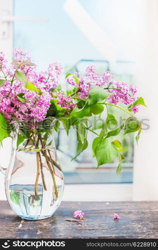 Lilac flowers bunch in glass vase on window still, indoor.