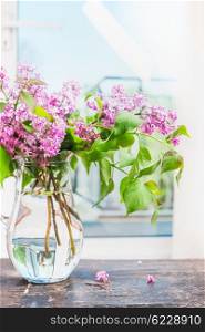 Lilac flowers bunch in glass vase on window still, indoor.