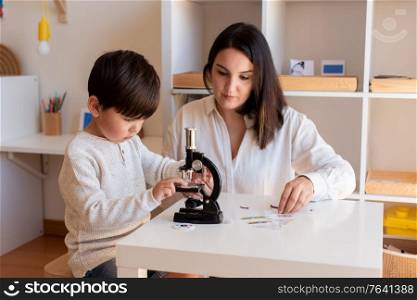 Lillte Kid exploring science with a microscope and mother or teacher help. Homeshooling. Learning Community. Montessori School